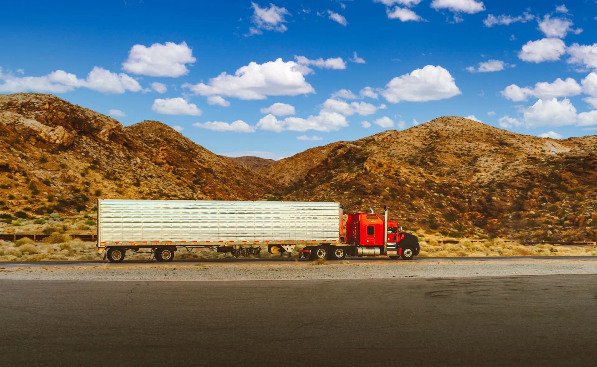 Eric Logistics red semi truck with refrigerated trailer crossing desert mountains